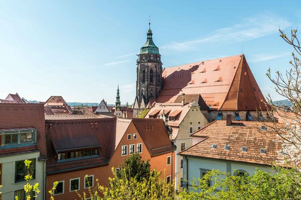 Historische Kirche in Pirna, von Gebäuden umgeben, blauer Himmel im Hintergrund.