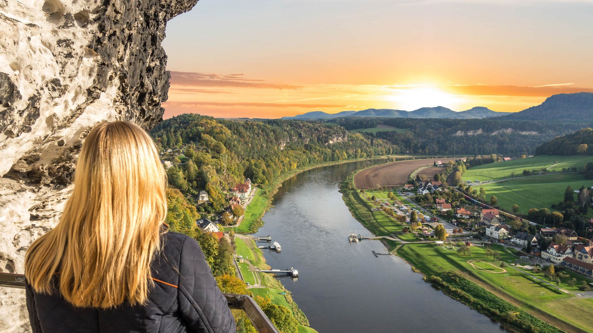 Sonnenuntergang über Rathen, Felsen und Bäume im Vordergrund, warmes Licht am Himmel.